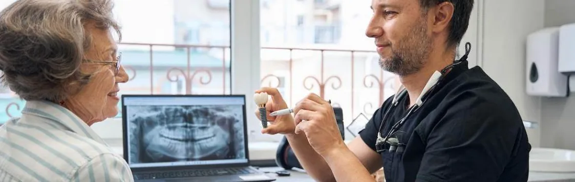 A dentist showing an older patient a dental implant beside her X-ray