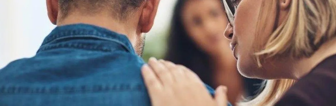 A woman resting a hand on a friend's shoulder to comfort him